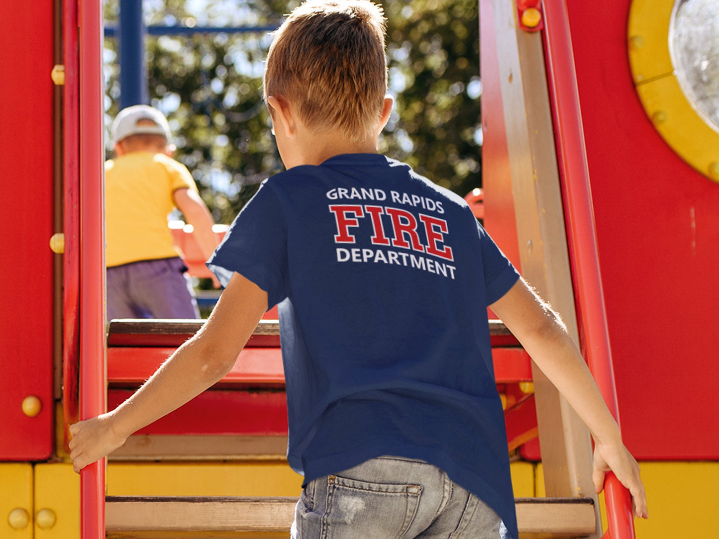 Boy looking out window wearing a navy blue T-shirt with grand rapids fire department in red and white on the back.
