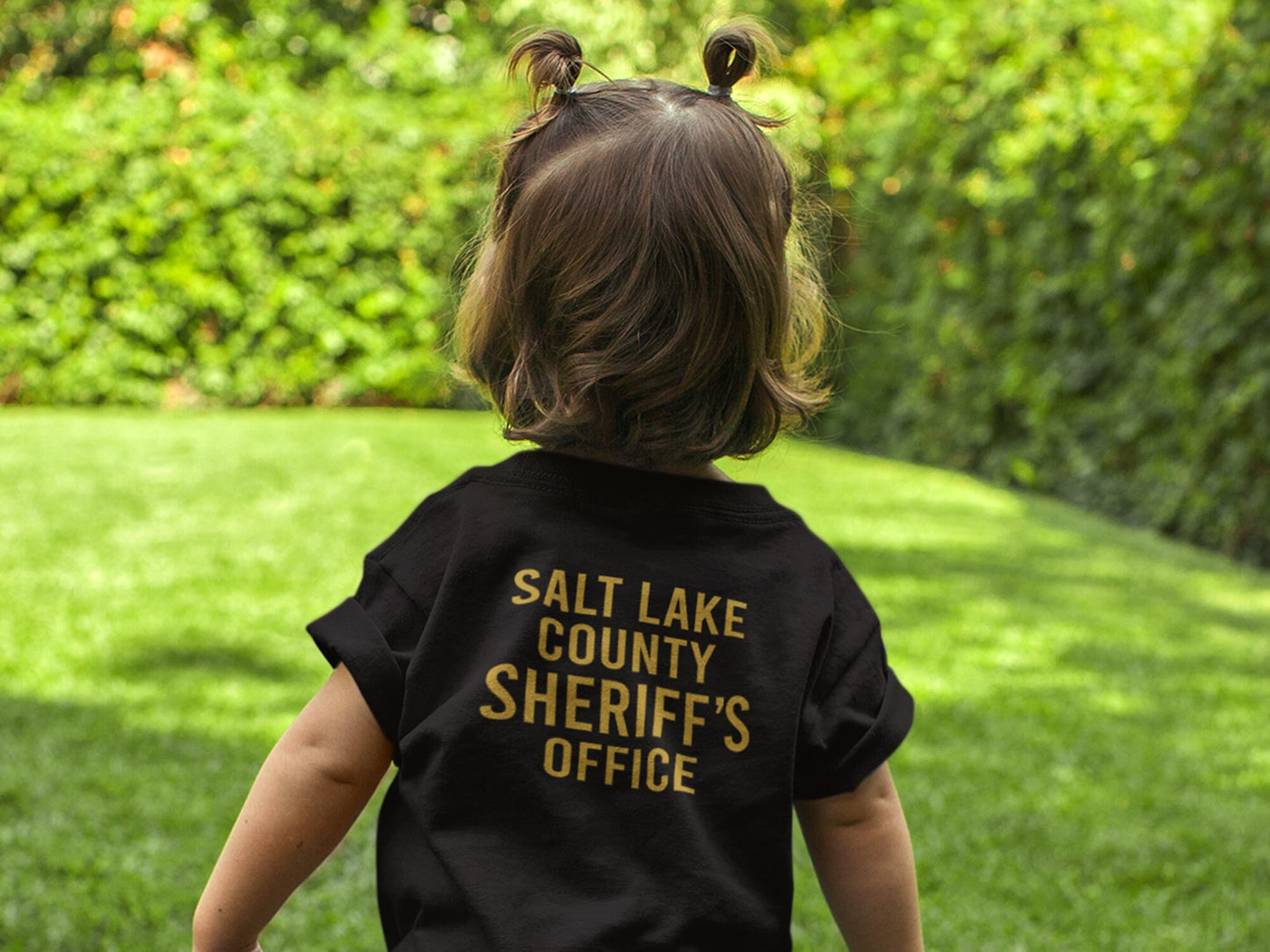 Back view of toddler wearing a black t-shirt with 'Salt Lake County Sheriff's Office' in gold lettering.