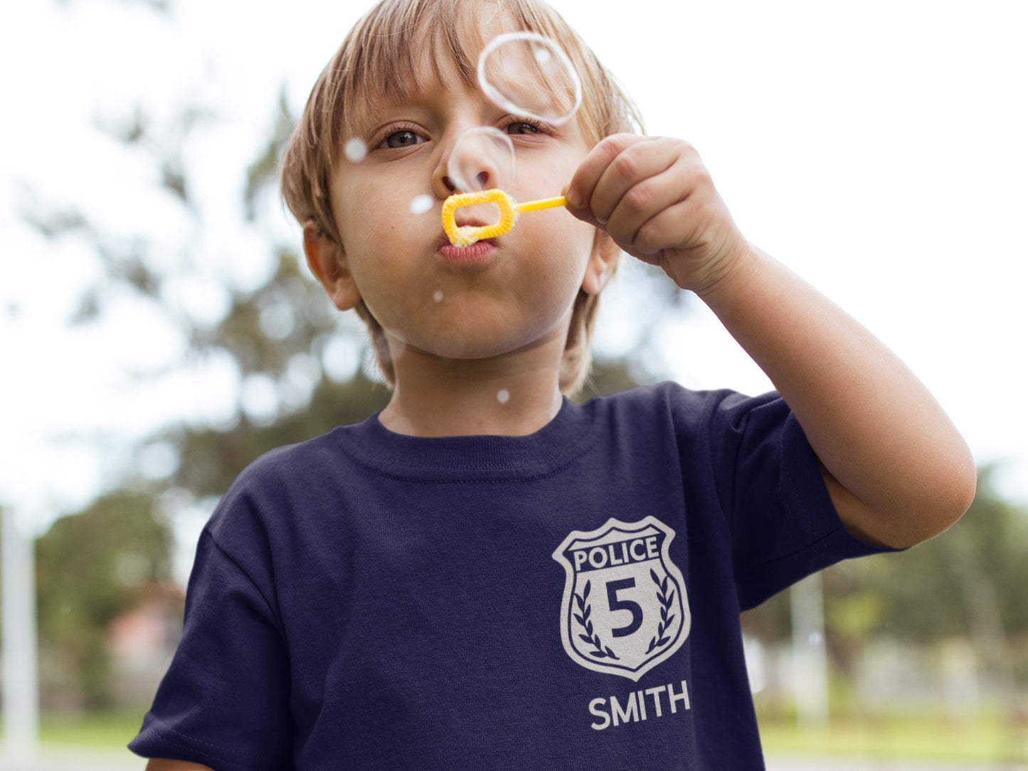Young child wearing a navy blue birthday police shirt. Silver police badge on left chest with number 5 and child's name "Smith" underneath.