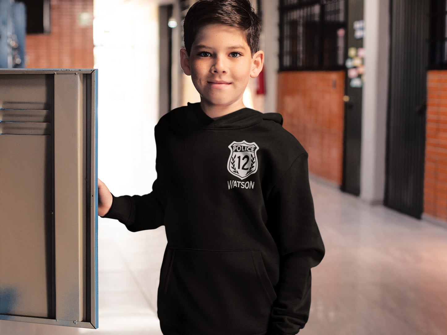 Black child-size hoodie sweatshirt with a white police badge graphic. The badge features the text 'POLICE' above the number '12' and 'WATSON' below. The hoodie has a drawstring hood and kangaroo pocket. The sweatshirt is a comfortable, casual style suitable for everyday wear.