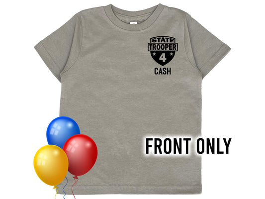 A gray t-shirt with a black state trooper patch on the front. The patch has a star on each side and the text 'STATE TROOPER' and 'CASH' below. The number '4' is in the center of the patch. Bright colored balloons indicate a birthday theme.