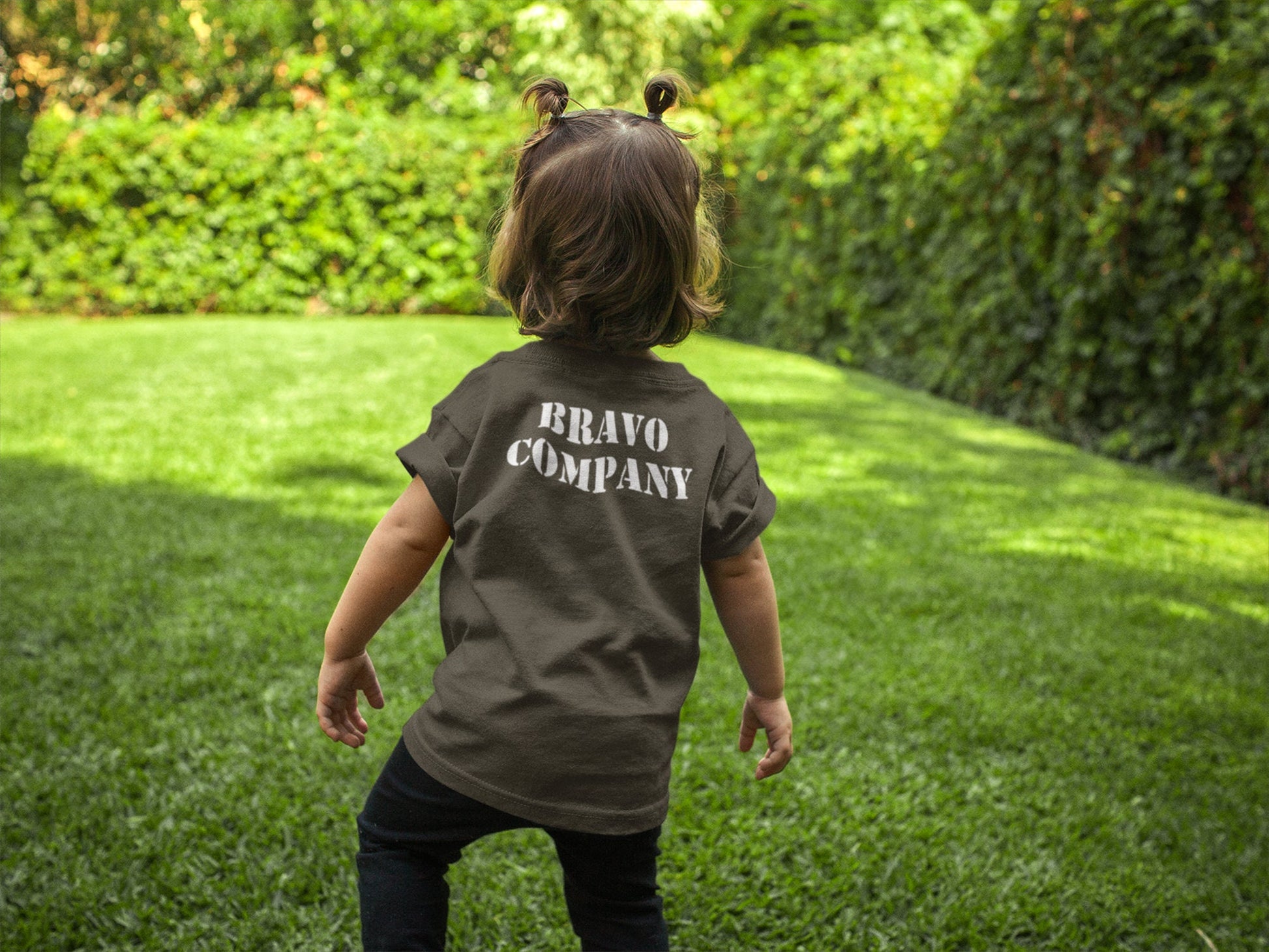 A small child wearing a military green t-shirt with the words &#39;BRAVO COMPANY&#39; printed in white on the back.