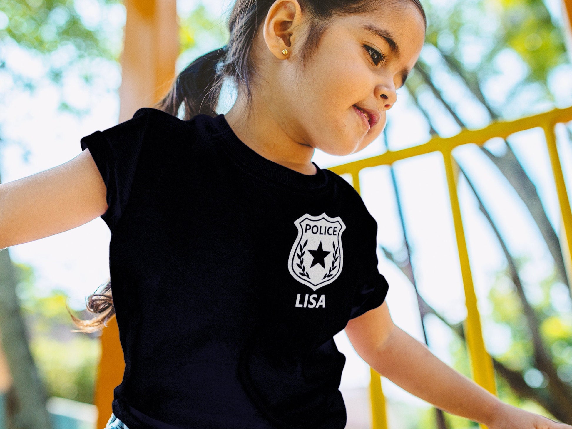 Young girl wearing a black t-shirt with a silver police badge design and the name &#39;LISA&#39; printed below it.