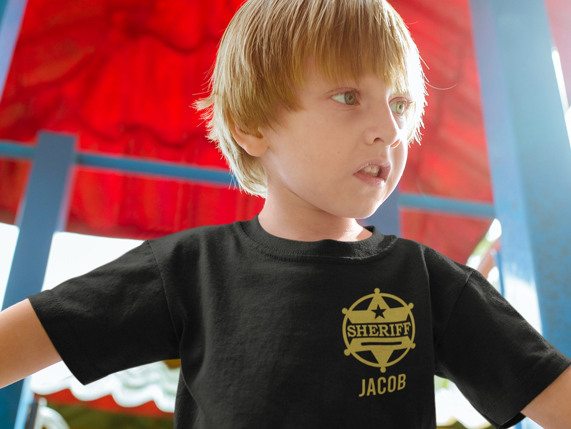 Young boy at playground wearing a short sleeve black t-shirt with gold Sheriff&#39;s badge on left chest and his name, Jacob, underneath.