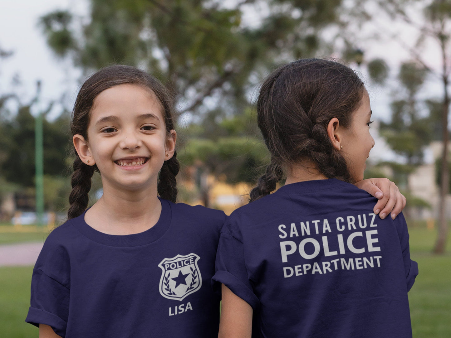 A child wearing a navy blue t-shirt with a silver police badge and the name &#39;LISA&#39; printed on the front. Another child showing back of the shirt has the text &#39;SANTA CRUZ POLICE DEPARTMENT&#39; printed in silver.