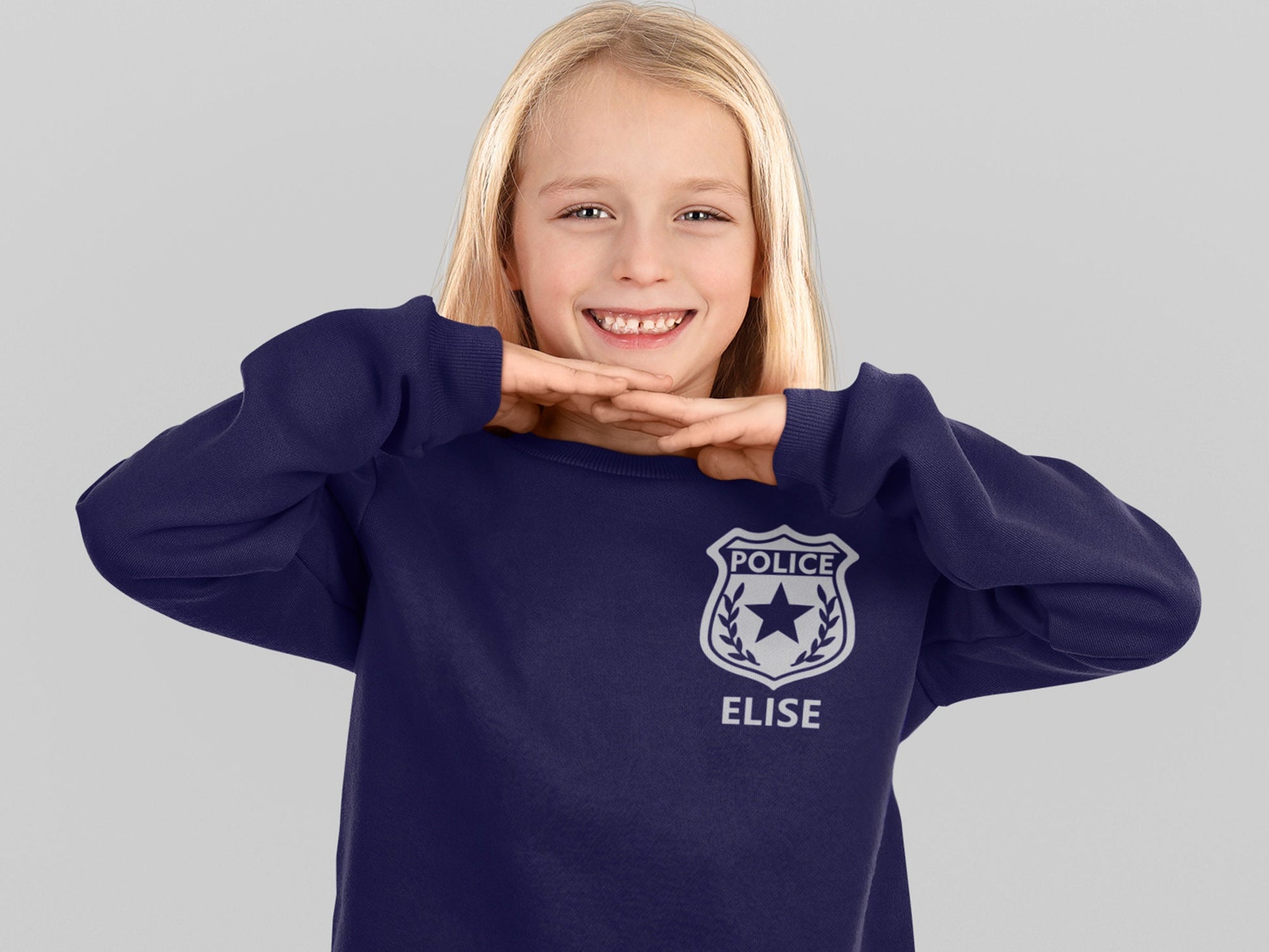 Girl wearing a navy blue sweatshirt with a silver police badge design and the name &#39;Elise&#39; printed below it in silver.