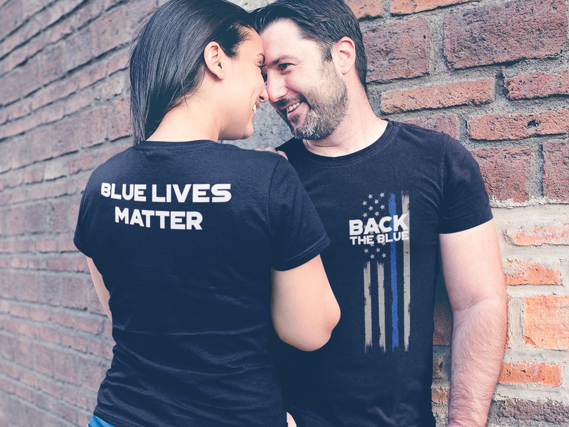 Two people wearing black t-shirts with white text. The person on the left is wearing a t-shirt that says &#39;Blue Lives Matter&#39;. The person on the right is wearing a t-shirt that says &#39;Back The Blue&#39; with a thin blue line American flag design.