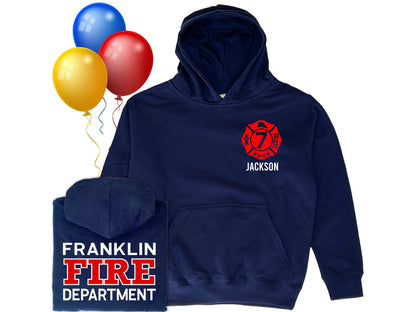 Navy blue hooded sweatshirt in youth sizes with custom red Maltese Cross on the front. Maltese Cross contains a custom number representing the youth&#39;s age. The youth&#39;s name is under the Maltese Cross. A folded hoodie shows a custom fire department name with &quot;Fire&quot; and &quot;Department&quot; written underneath. Three colorful balloons indicate a birthday theme.