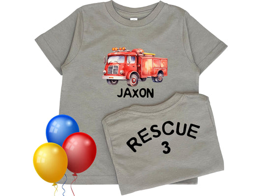 Kid&#39;s gray short sleeve T-shirt with watercolor style firetruck on the front chest and &quot;Jaxon&quot;, representing personalized name underneath. The back of the shirt displays the number &quot;3&quot; representing the child&#39;s custom age.