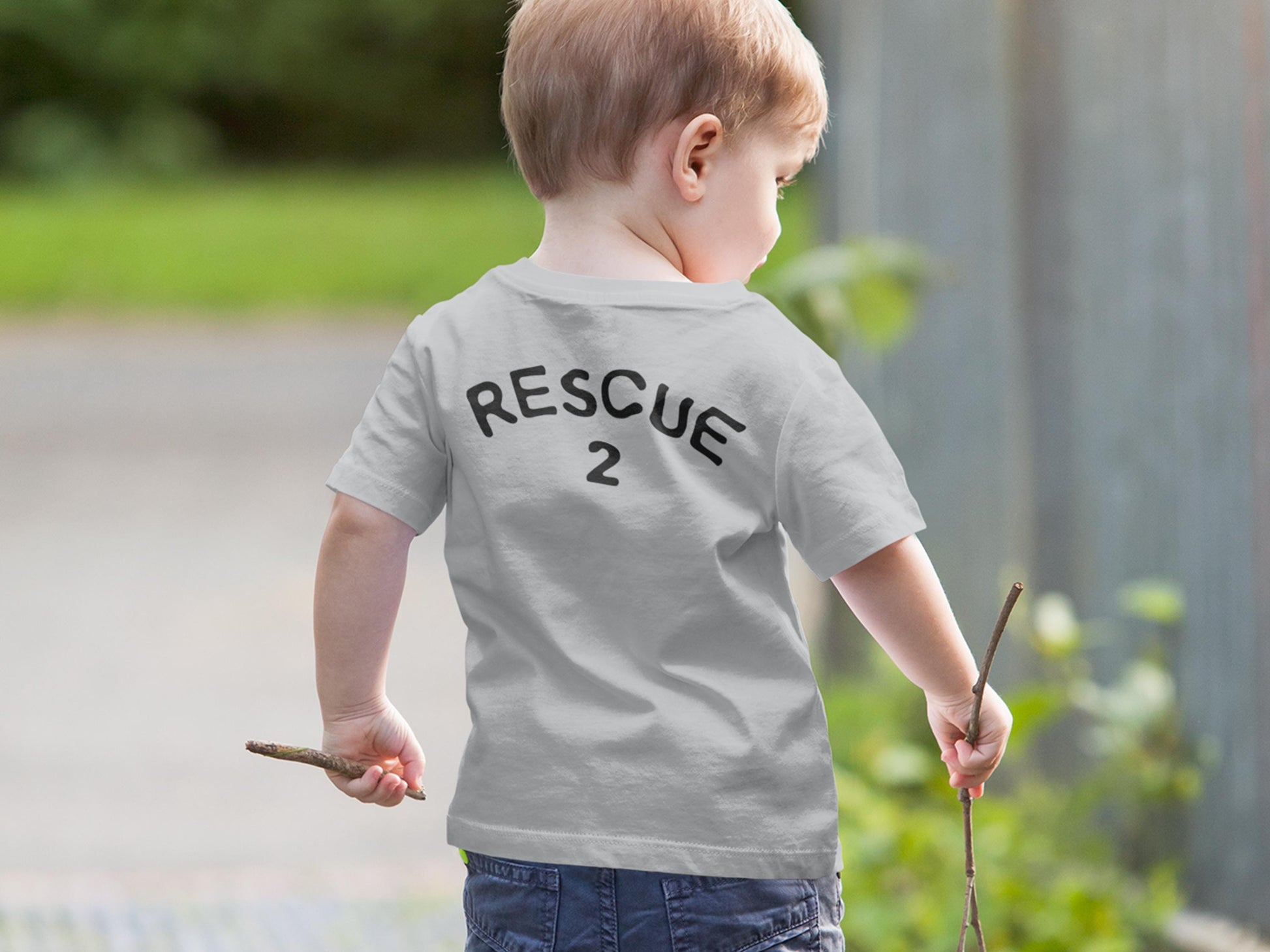 Back view of small boy holding sticks in each hand, wearing a gray short sleeve t-shirt that says &quot;Rescue&quot; and the number &quot;2&quot; as placeholders for custom text and age.