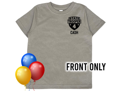 A gray t-shirt with a black state trooper patch on the front. The patch has a star on each side and the text &#39;STATE TROOPER&#39; and &#39;CASH&#39; below. The number &#39;4&#39; is in the center of the patch. Bright colored balloons indicate a birthday theme.